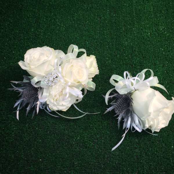Two white rose corsages with ribbon and dark feather accents on green turf