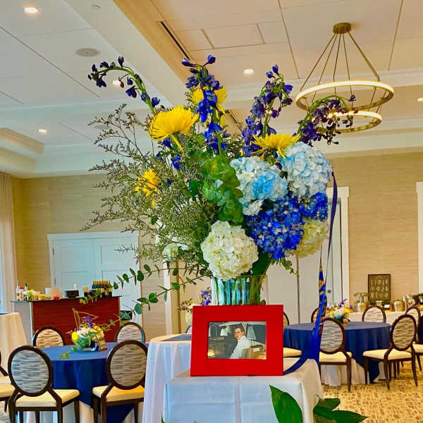 Tall floral centerpiece with blue, yellow, and white blooms in a vase