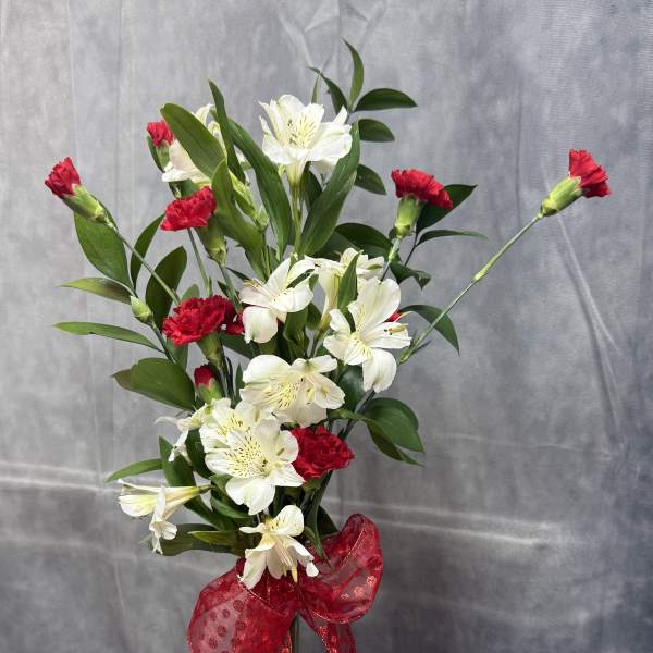White alstroemeria and red carnations in a clear glass vase with a red bow.