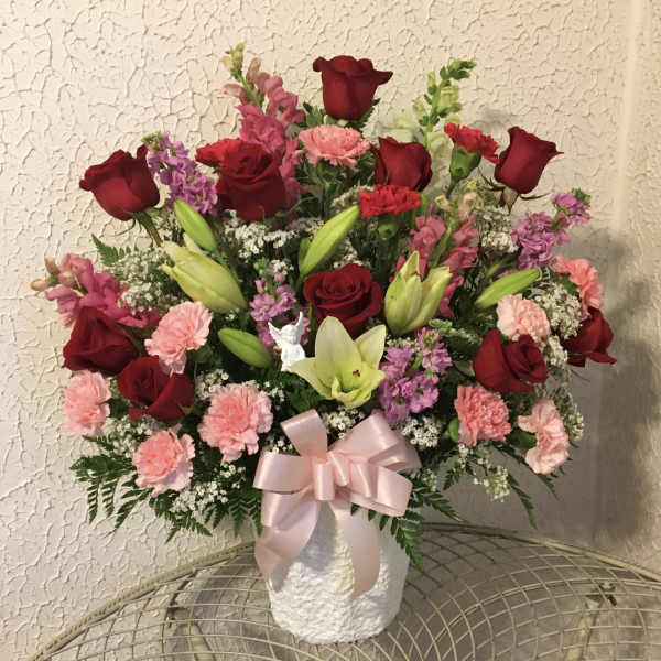 Bouquet of red roses, pink carnations, and lilies in a white vase with a pink ribbon