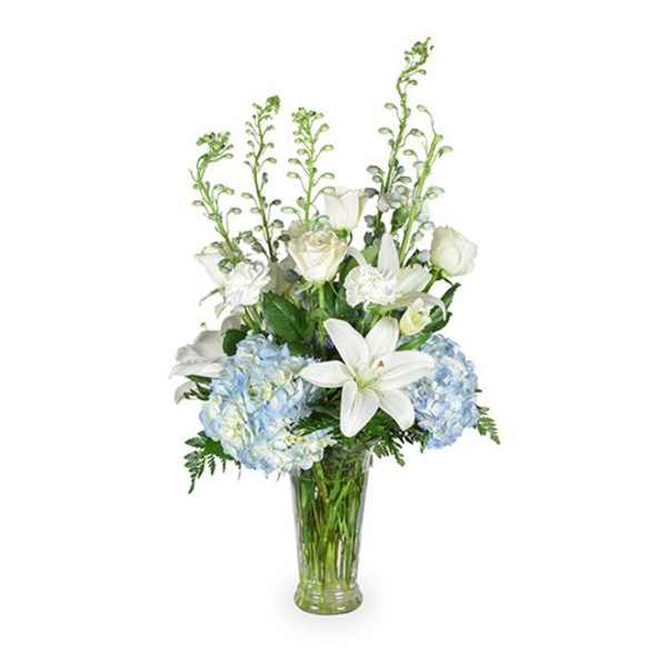 White lilies and blue hydrangeas in a clear glass vase