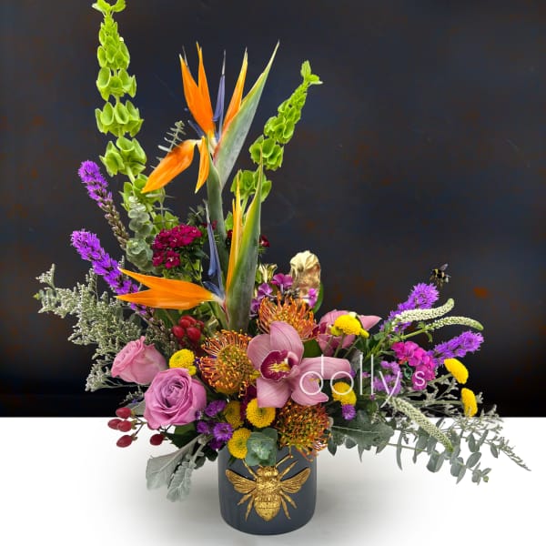 Tropical floral arrangement in a dark vase with a gold bee accent