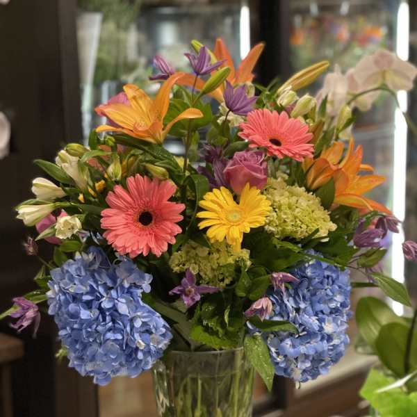 Colorful mixed bouquet in a clear glass vase with blue hydrangeas and gerbera daisies