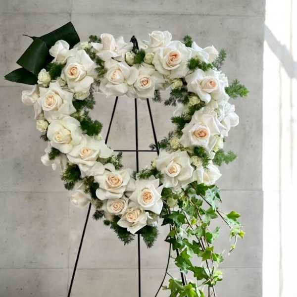 Heart-shaped wreath of white roses with trailing ivy on a black easel stand