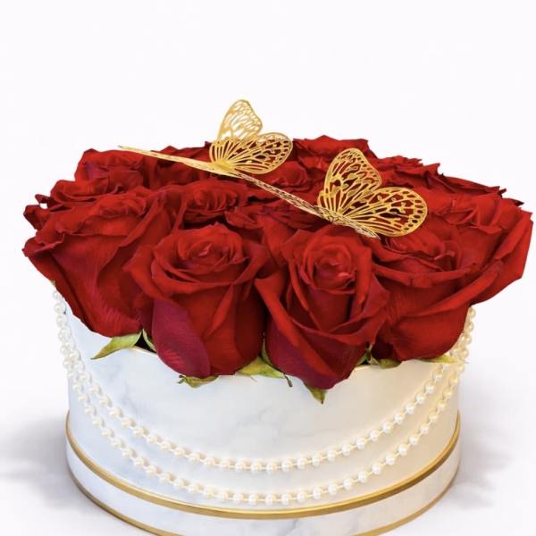 Round box of red roses topped with gold butterfly decorations