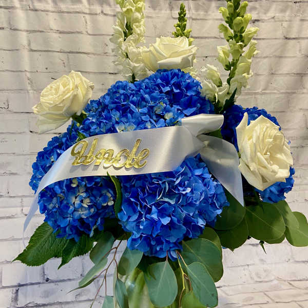 Blue hydrangea and white rose arrangement in a glass vase with a white ribbon