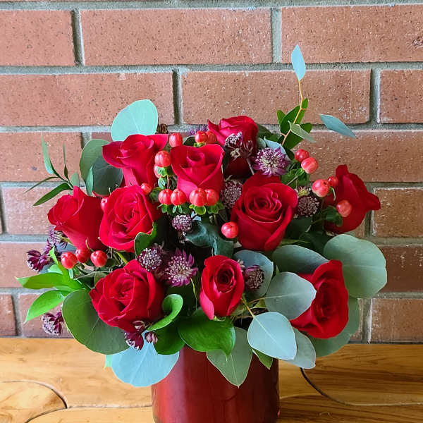 Red roses arranged in a red vase with eucalyptus and small accent flowers