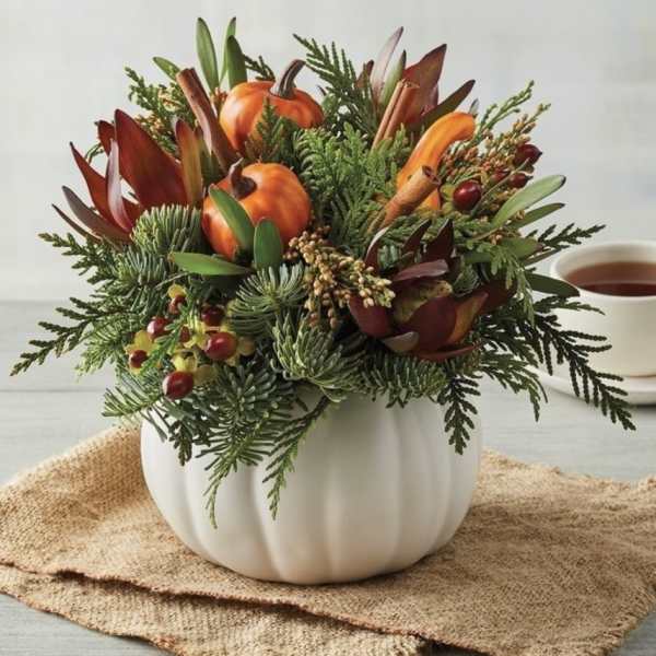 Autumn floral arrangement in a white pumpkin vase with orange pumpkins