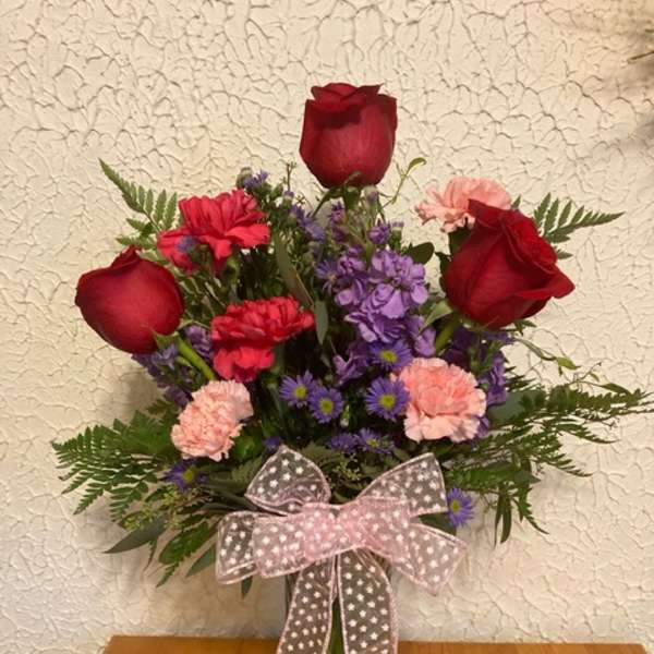 Bouquet of red roses, purple flowers, and pink carnations in a glass vase with a ribbon