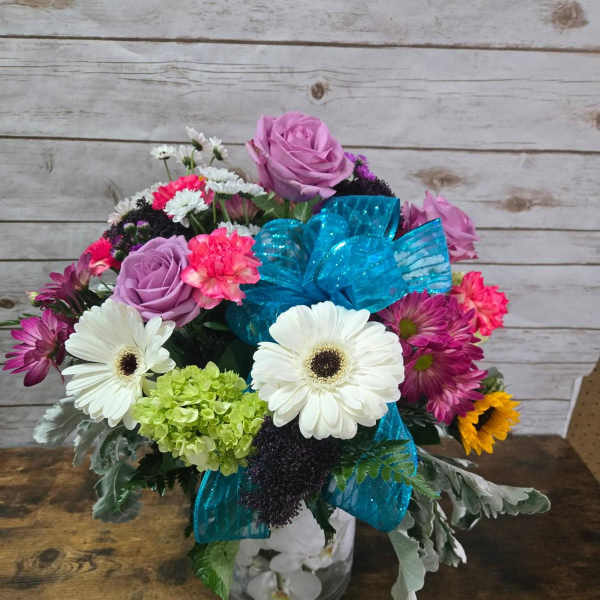 Mixed bouquet with roses, daisies, and a blue ribbon in a glass vase