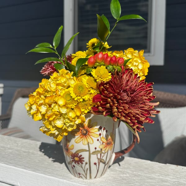 Yellow and red chrysanthemum arrangement in a floral mug vase