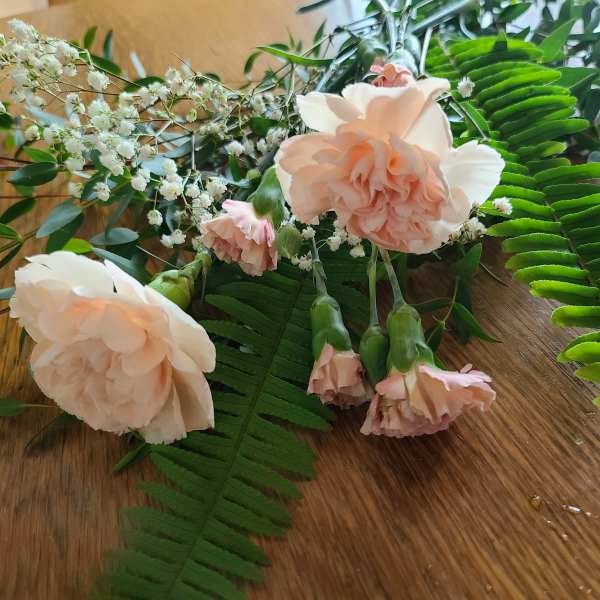 Peach carnations with baby's breath and fern fronds on a wooden surface