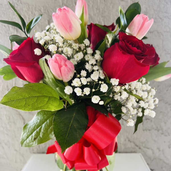 Bouquet of red roses and pink tulips in a glass vase with a red ribbon