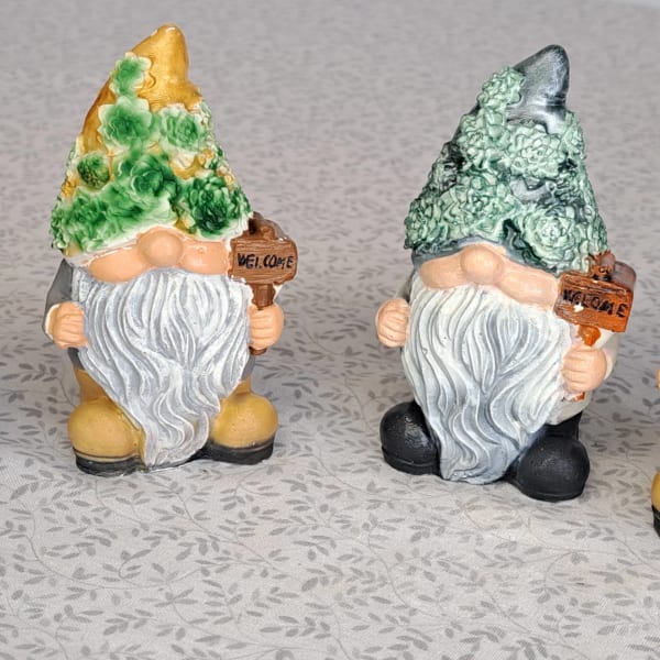 Set of four garden gnome figurines with flower-textured hats holding welcome signs