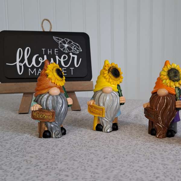 Four small gnome figurines holding sunflowers and welcome signs