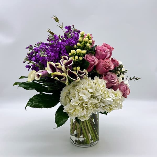 Mixed bouquet of purple, pink, and white flowers in a clear glass vase