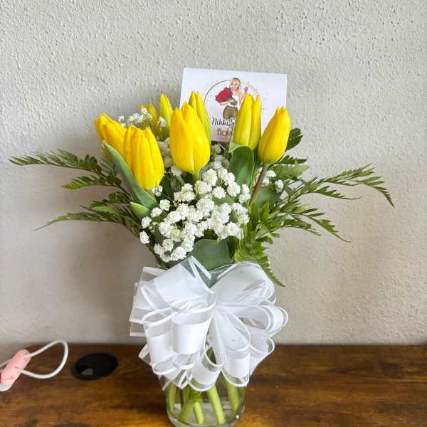 Yellow tulips in a glass vase with white baby's breath and a white ribbon bow