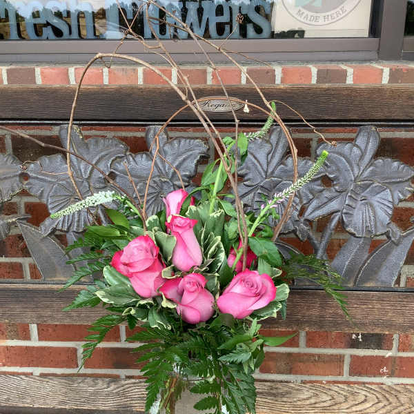 Pink roses arranged in a glass vase with branches and greenery