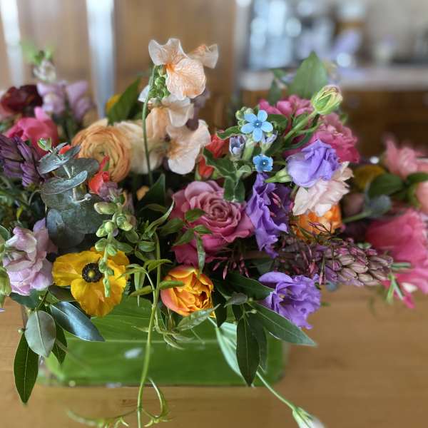 Mixed bouquet of purple, pink, peach, and yellow flowers in a glass vase