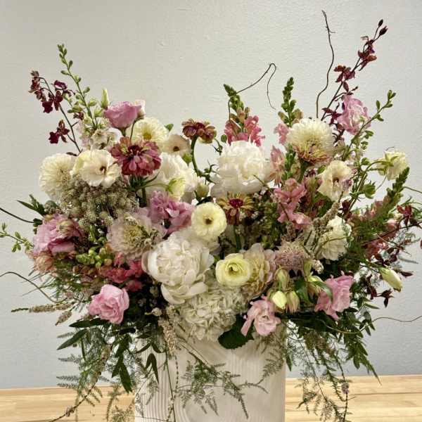 Large airy arrangement of white and pink flowers with burgundy accents in a tall white ceramic vase.