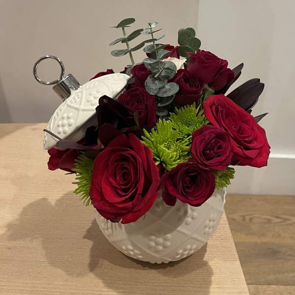 Red roses in a white textured ornament-shaped vase with greenery