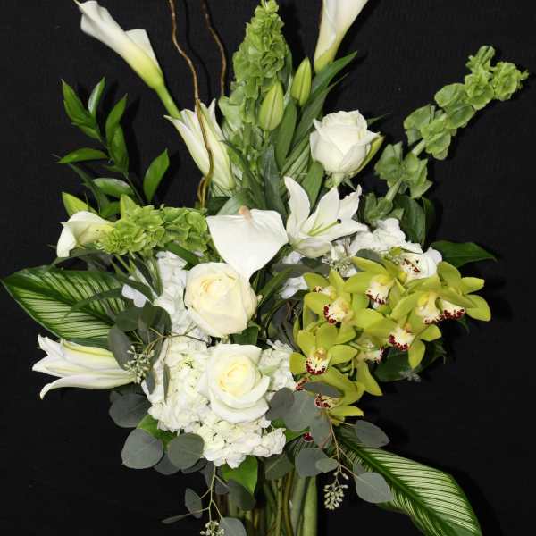White floral arrangement with orchids, roses, and calla lilies in a glass vase