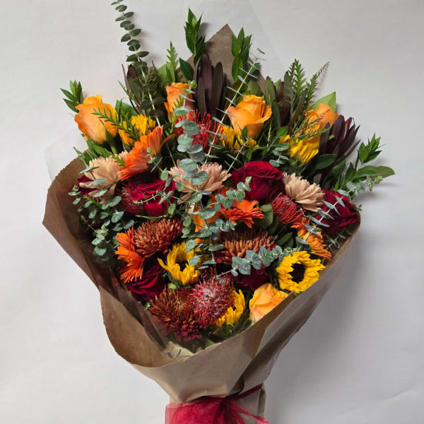 Mixed bouquet of orange, red, and yellow flowers wrapped in brown paper