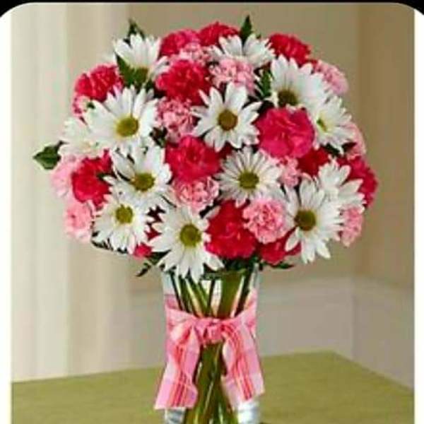 Bouquet of white daisies and pink carnations in a glass vase with a pink ribbon