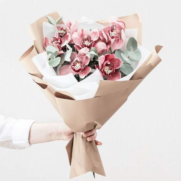 Bouquet of pink orchids wrapped in tan and white paper