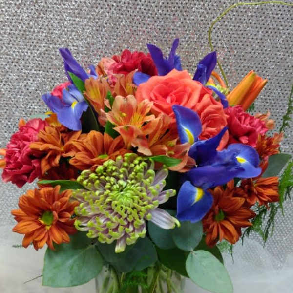 Mixed bouquet of orange, pink, and blue flowers in a glass vase