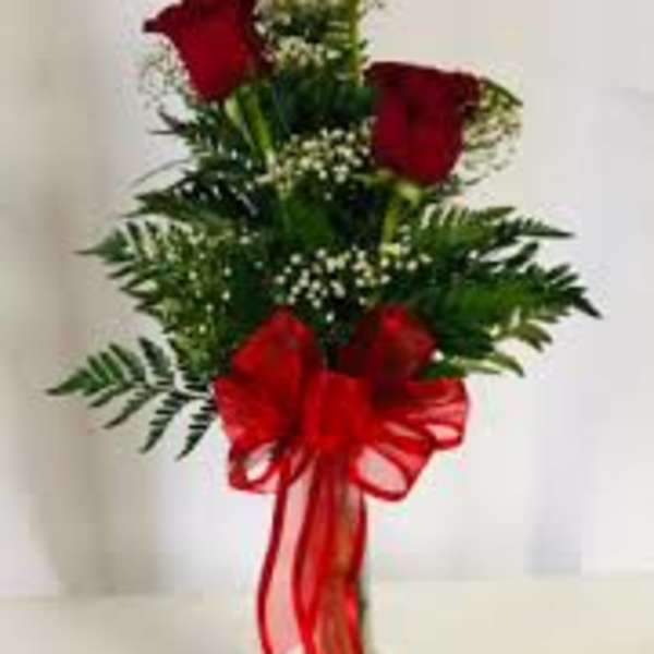 Red roses arranged in a clear vase with a large red bow