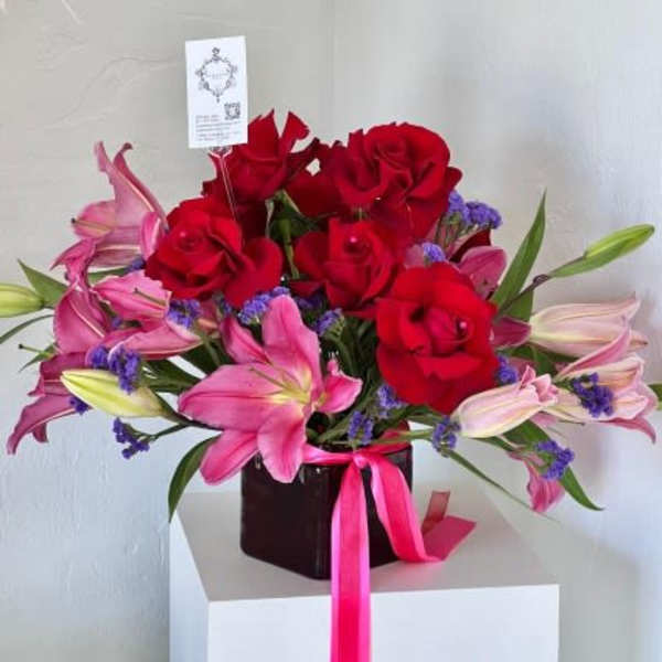 Red roses and pink lilies in a dark vase with a pink ribbon