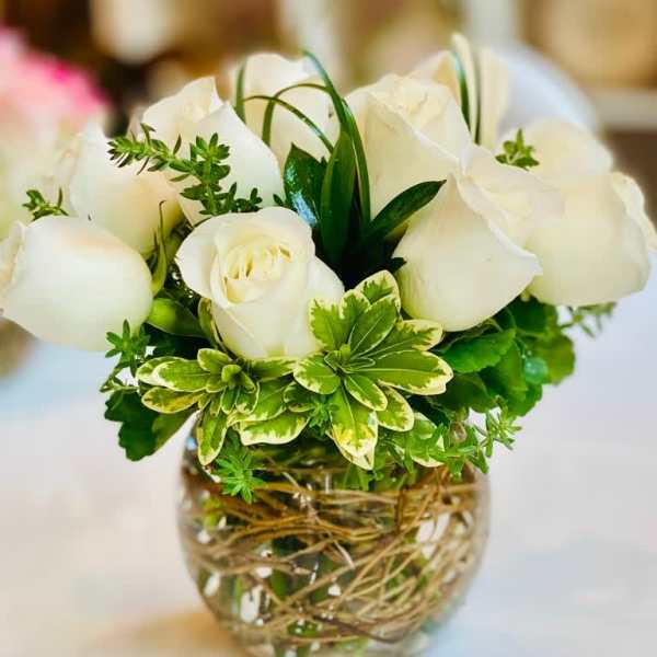 White roses arranged in a clear glass vase with green foliage