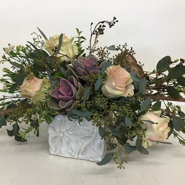 Low floral arrangement with roses, succulents, and greenery in a white vase