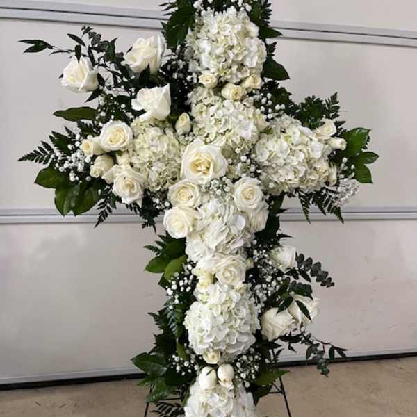 White floral cross arrangement with roses and hydrangeas on a stand
