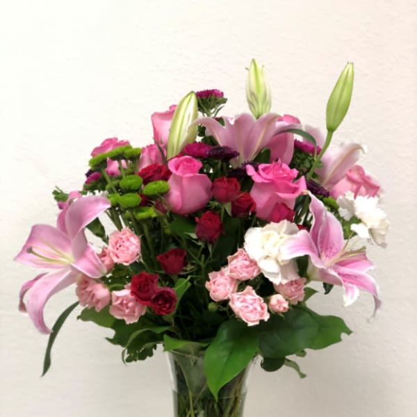 Pink lilies and roses arranged in a clear glass vase