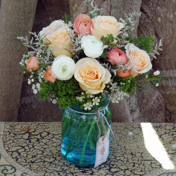 Peach and white roses with ranunculus and filler flowers arranged in a blue glass mason jar