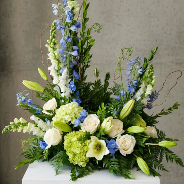 Tall floral arrangement with white roses, blue flowers, and green lilies