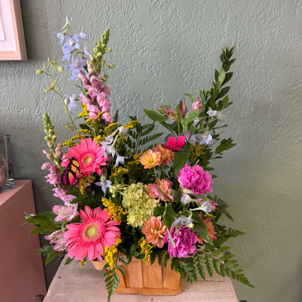 Colorful mixed flower arrangement in a wooden basket with butterfly picks