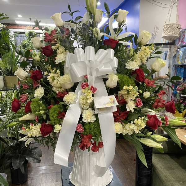 Large standing floral spray with red and white flowers and a white ribbon bow