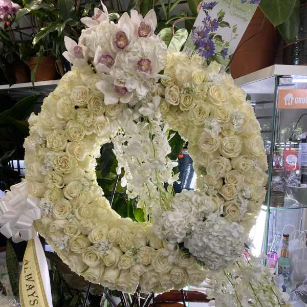 Large white floral wreath with orchids and roses on a stand