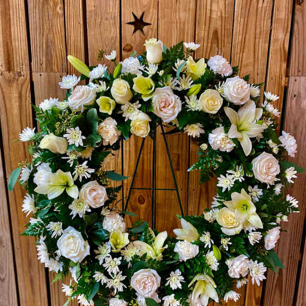 White floral wreath on a metal stand with roses and lilies