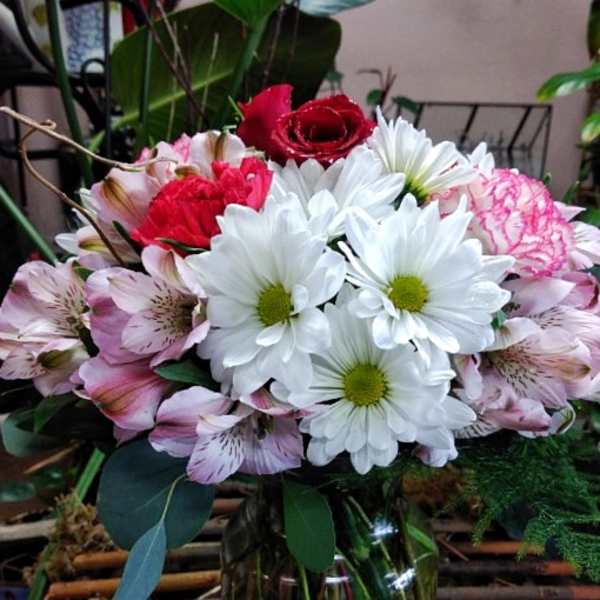 Mixed bouquet of white daisies, pink alstroemeria, and red roses in a glass vase