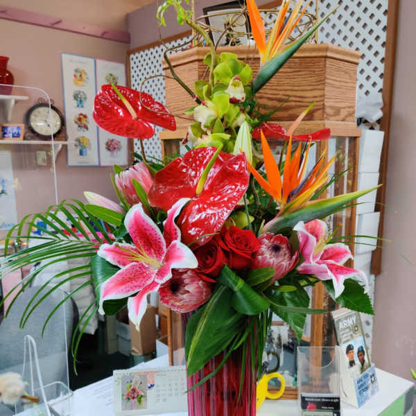 Tropical bouquet with red anthuriums, pink lilies, and orange bird-of-paradise in a red vase