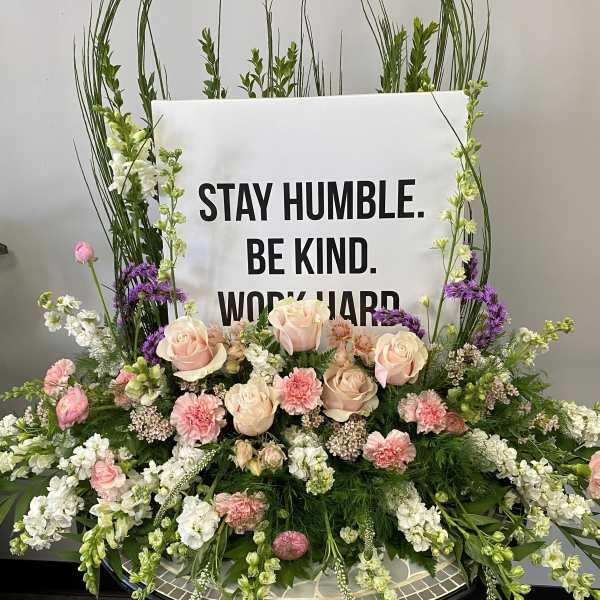 Large floral arrangement with a sign reading "STAY HUMBLE. BE KIND. WORK HARD."