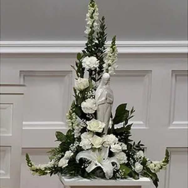 Tall white floral arrangement with lilies and roses around a statue