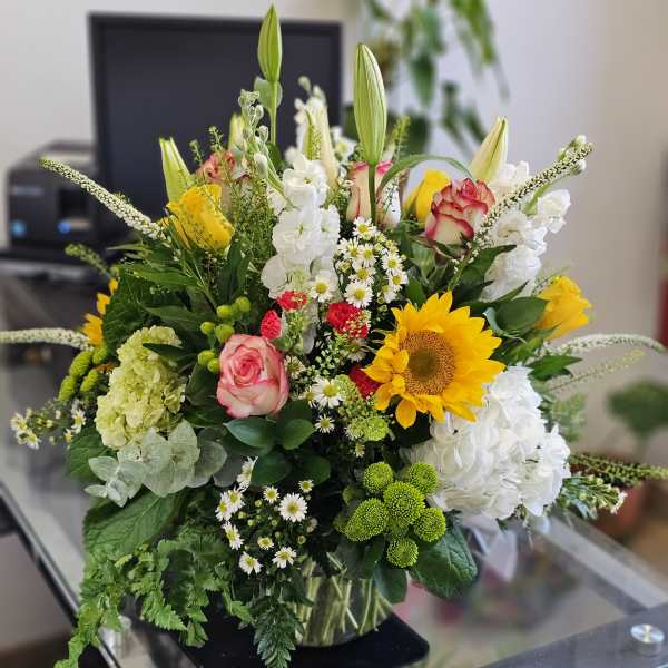 Mixed bouquet with sunflowers, roses, lilies, and white blooms in a glass vase