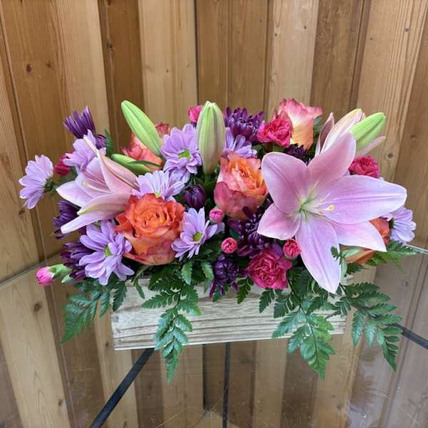 Low arrangement of pink lilies, orange roses, and purple mums in a rustic wooden box
