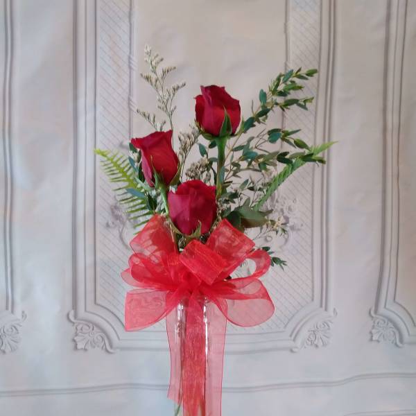 Three red roses in a clear glass vase with a large red bow