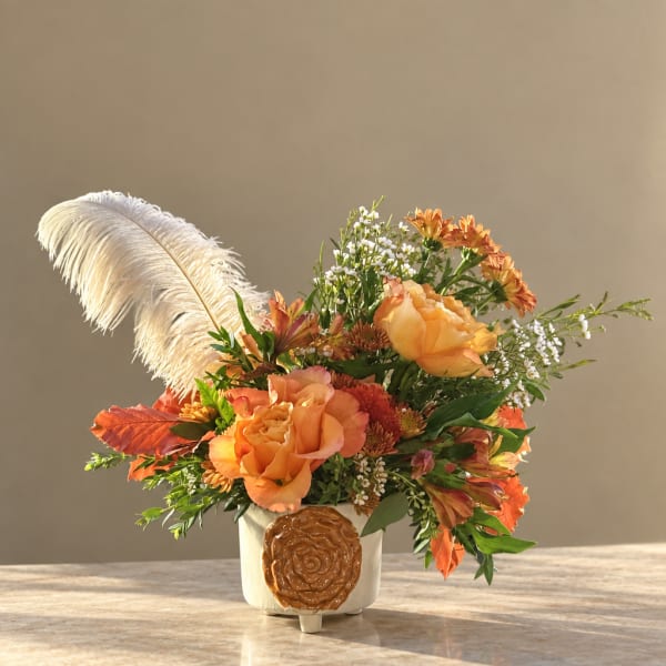 Orange floral arrangement in a white vase with a large white feather